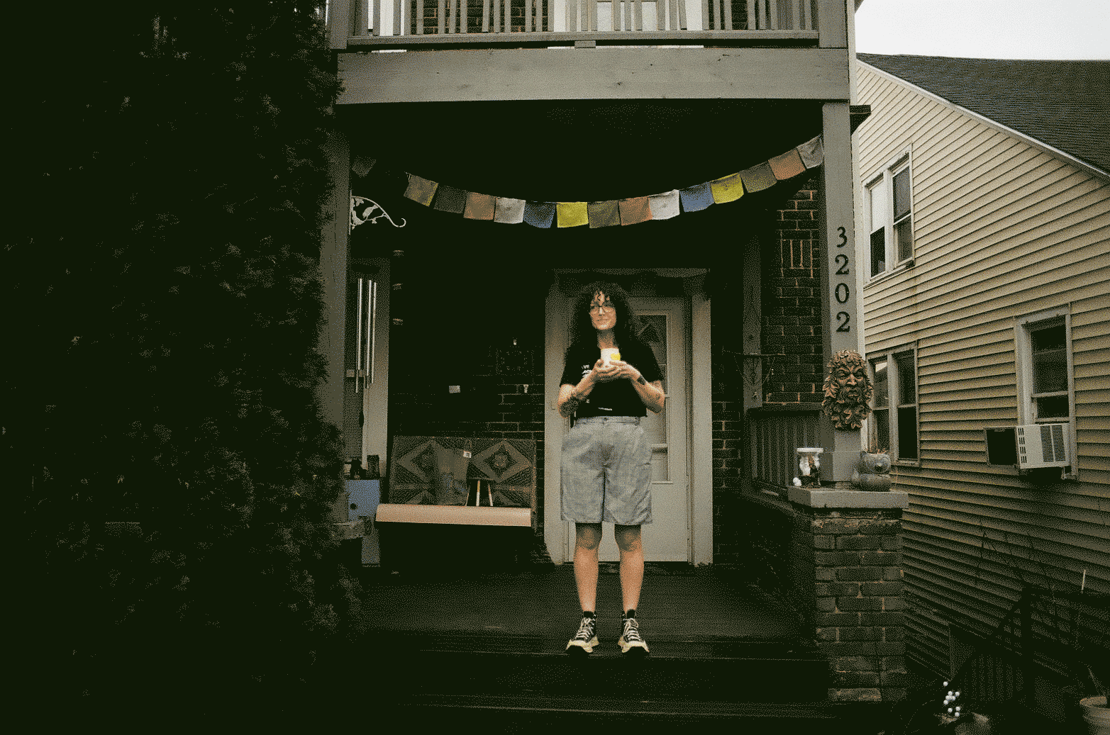 Woman standing on the porch holding a cup of coffee under a multicolor flag