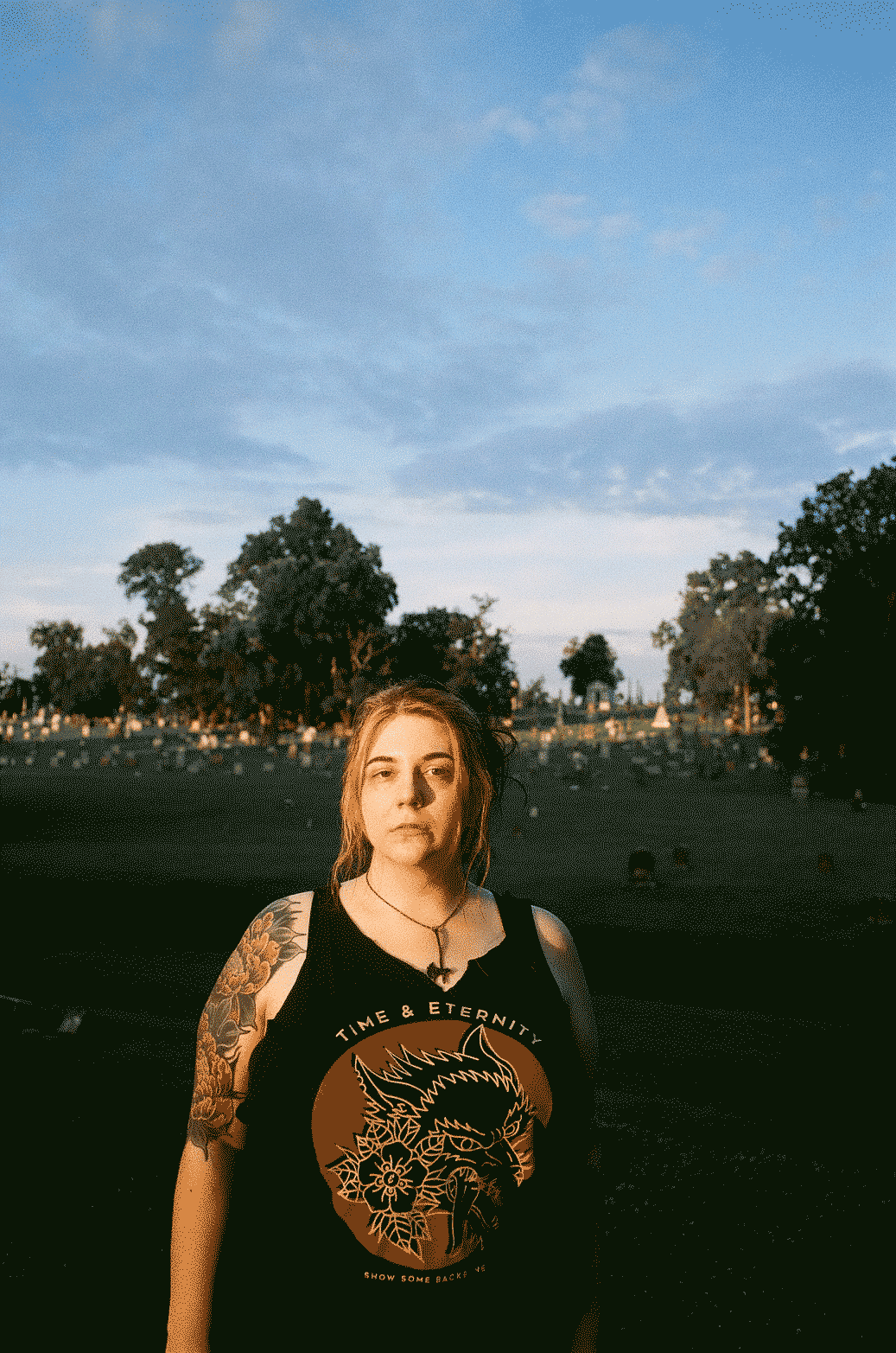 Woman standing looking at the camera in evening light with graves in the distance