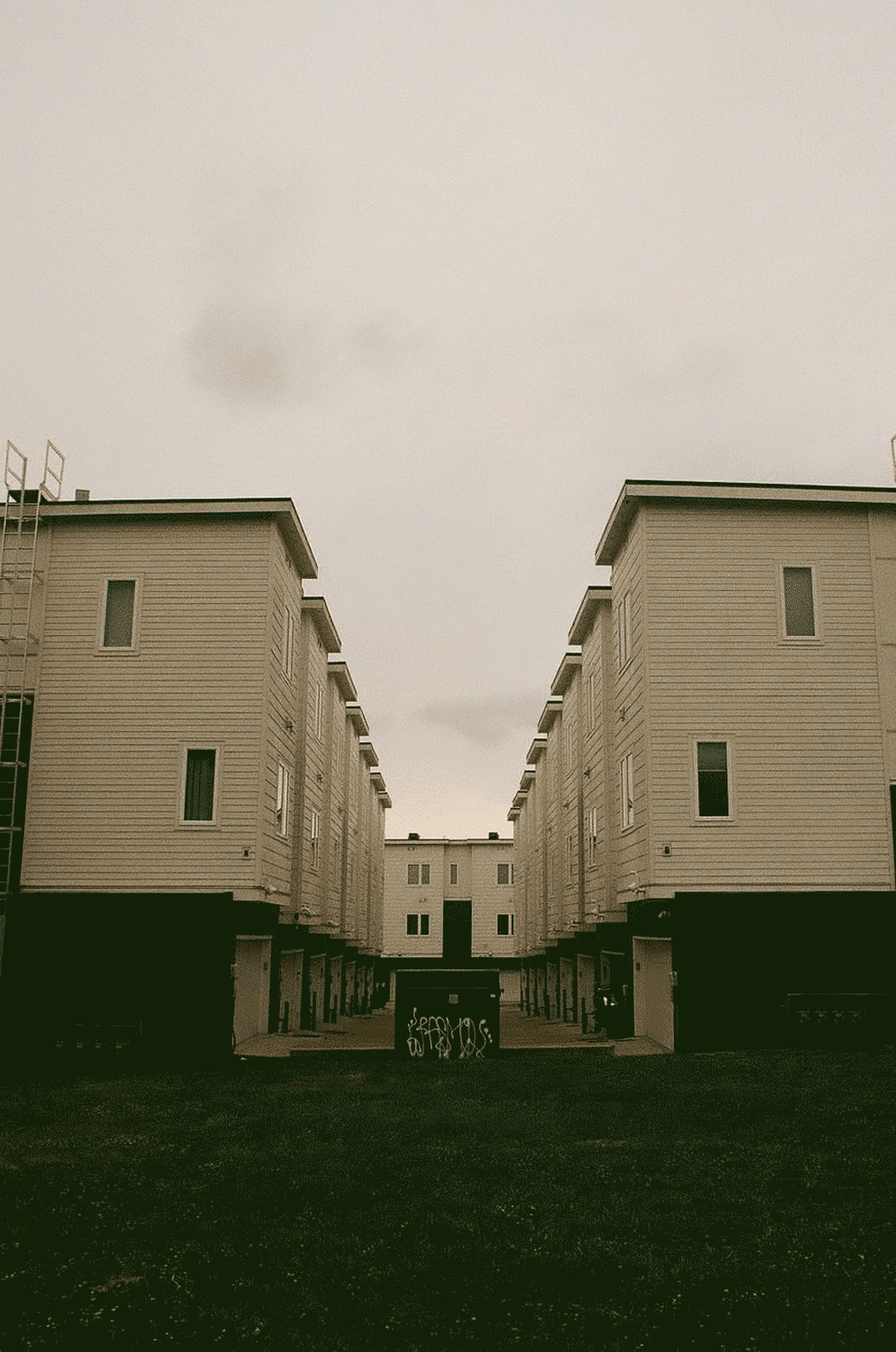 Symmetrical rows of plain buildings with a graffitied dumpster in the middle