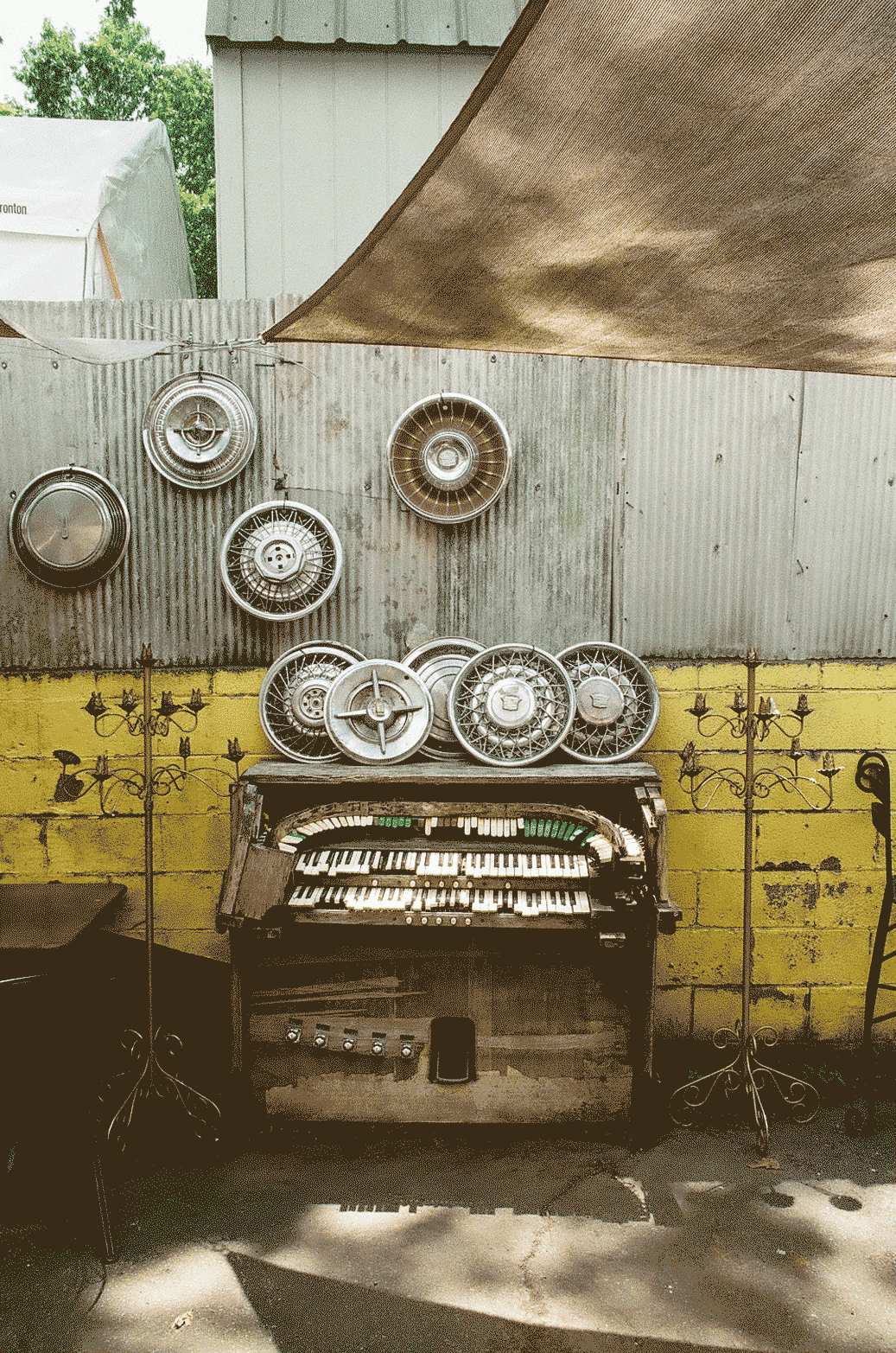 Old organ sitting outside with car hubcaps sitting on and around it