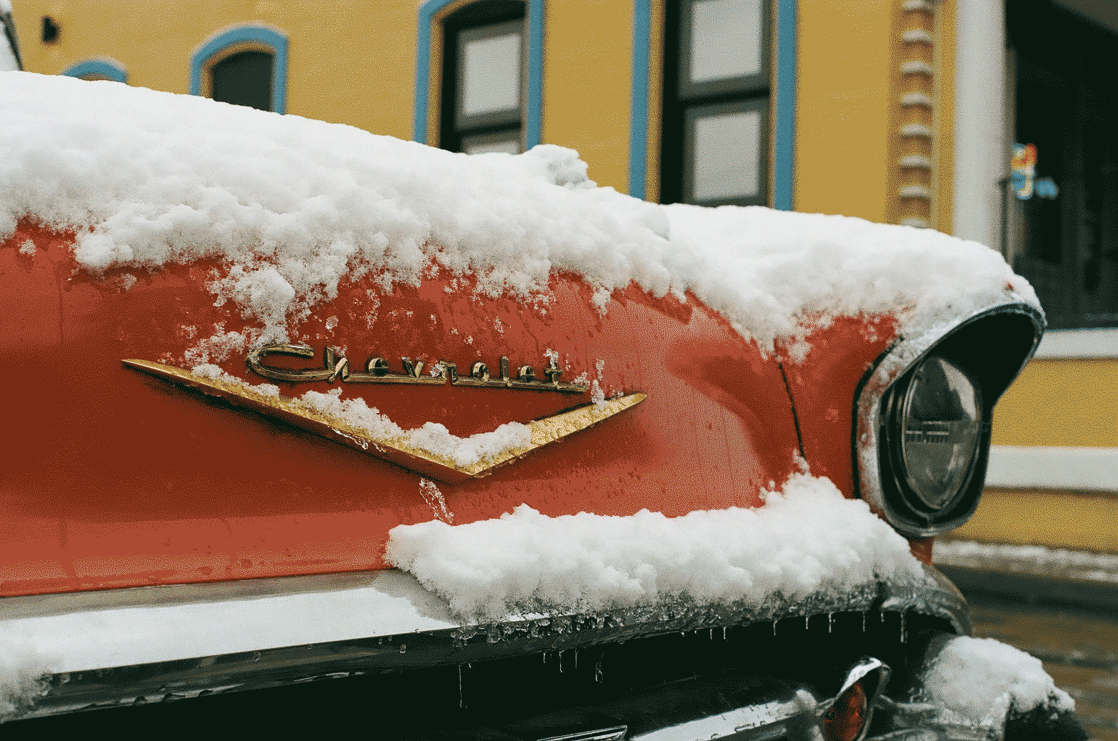 Classic red chevrolet car in front of a yellow building, fresh snow and ice covering the top